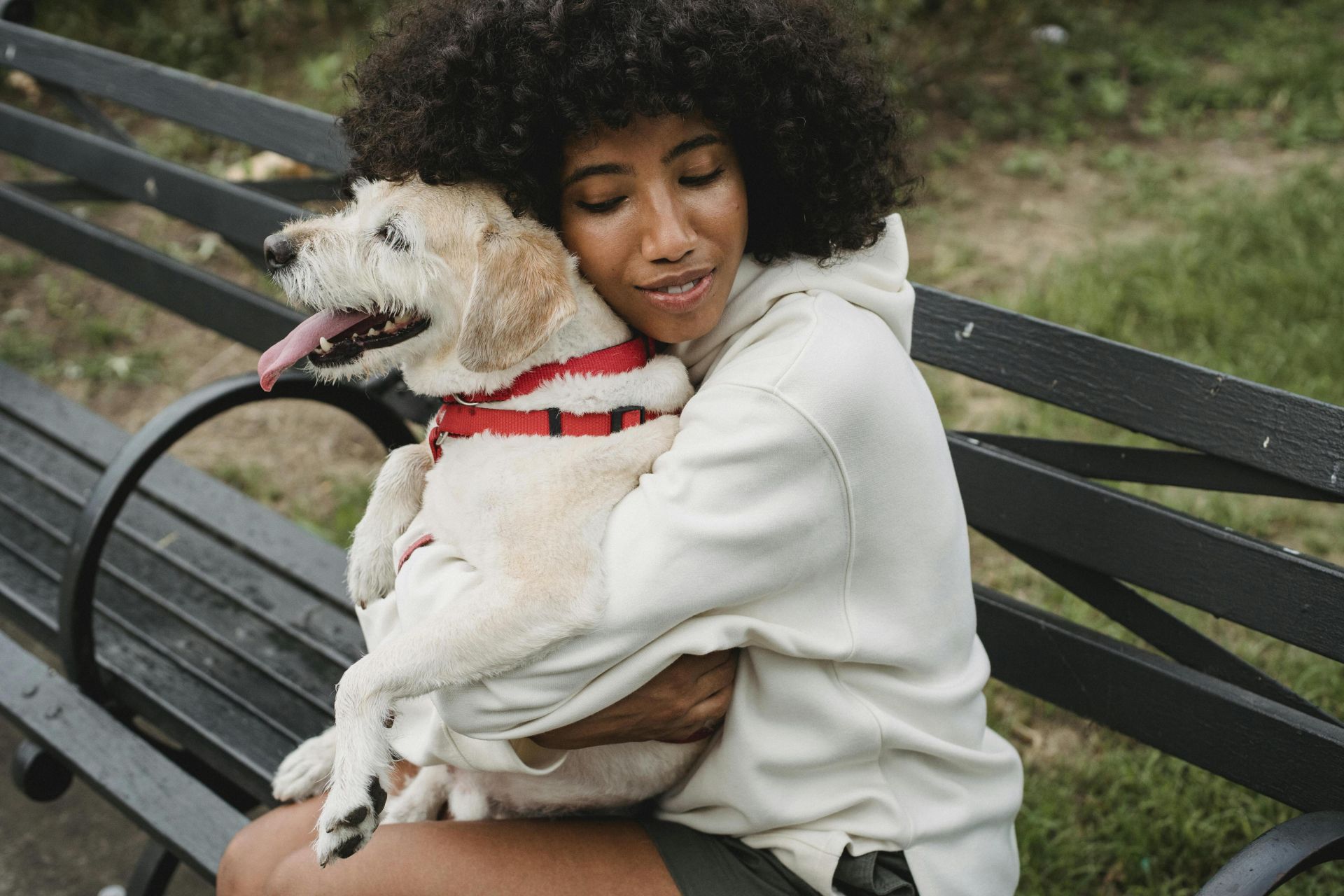 A woman with curly hair embracing her dog on a park bench, capturing pure affection and joy.